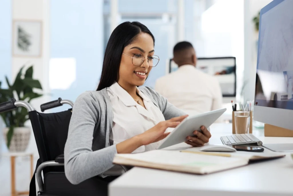 Disabled woman in wheelchair sitting at desk using tablet