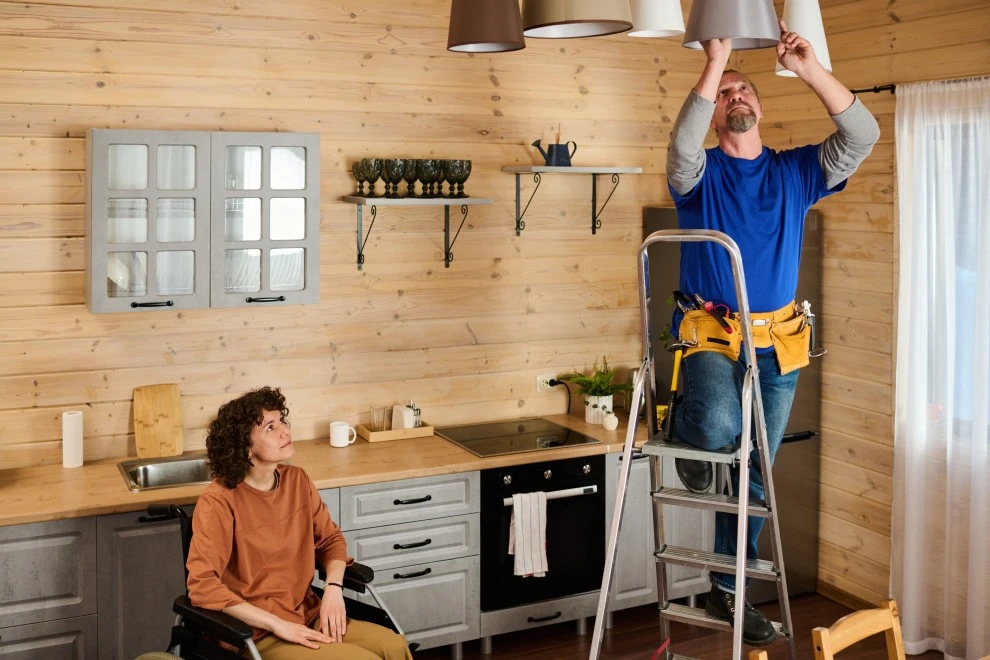 Man changing light on ladder for disabled woman who is sitting in wheelchair