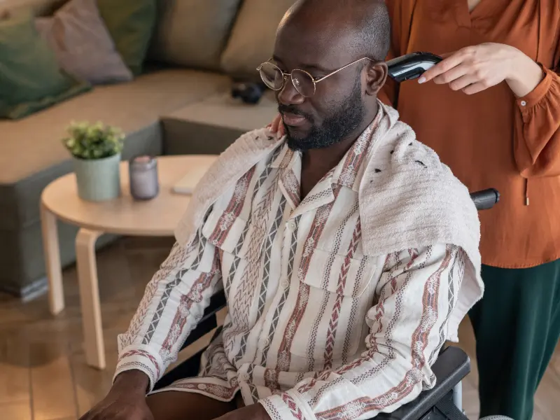 Disabled man in wheelchair having hair clipped by support worker