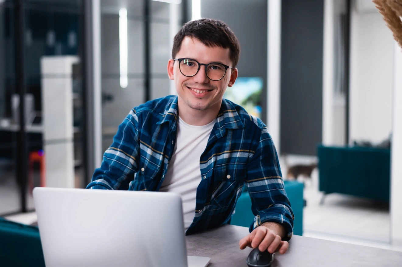Man sitting at desk smiling at camera with laptop in front of him