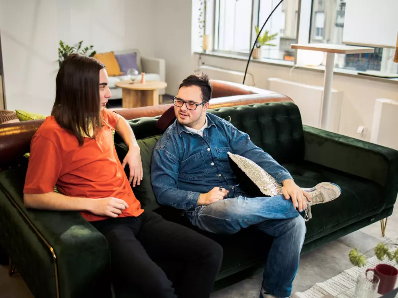 Disabled man with down syndrome sitting on couch talking with friend